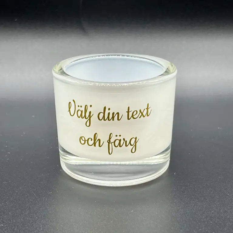 Expresspresenter.se:s Vit Ljuslykta | Välj din text är en genomskinlig ljusstake med vita frostade sidor och svensk text i guld, så att du kan välja ditt eget budskap - perfekt som en personlig gåva för alla utrymmen.