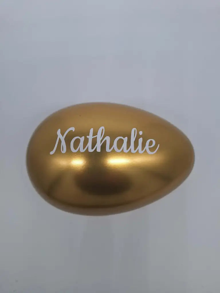 En 15 cm hög, guldglänsande Påskägg personligt från Expresspresenter.se, personifierad med "Nathalie" i elegant vit stil, visas mot en vanlig ljus bakgrund.