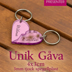 Två rosa "Nyckelring - Halvt hjärta i spegelplast (rosa)" från Express-presenter, med namnen Vilma och Emilie, länkas ihop på träyta. Text: Unik Gåva 4x3cm, 3mm tjock spegelplast.