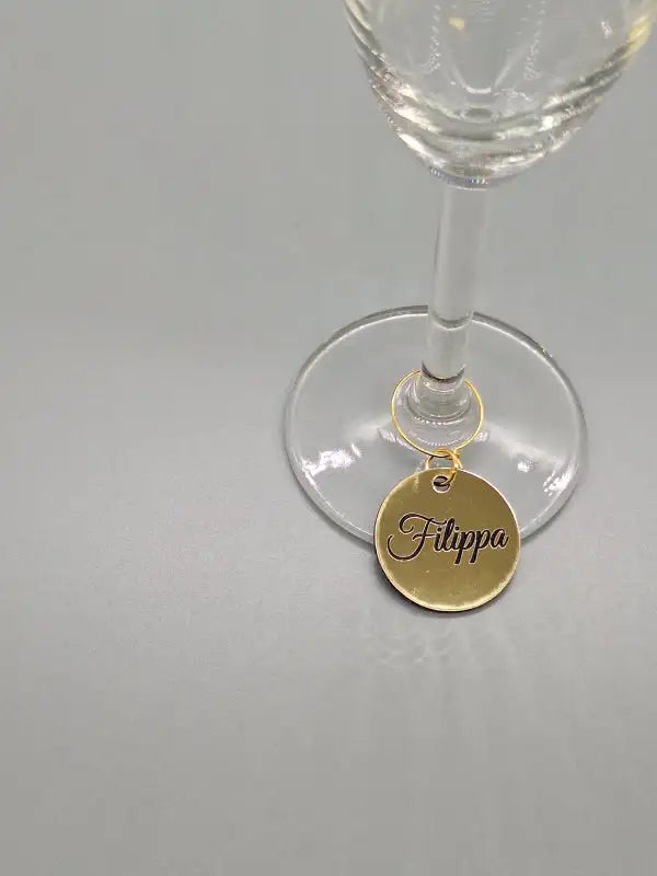 På en grå yta vilar ett klart vinglas med ett Expresspresenter.se Glasmarkör namn i guld, graverat med "Filippa" och elegant hängande på stjälken.