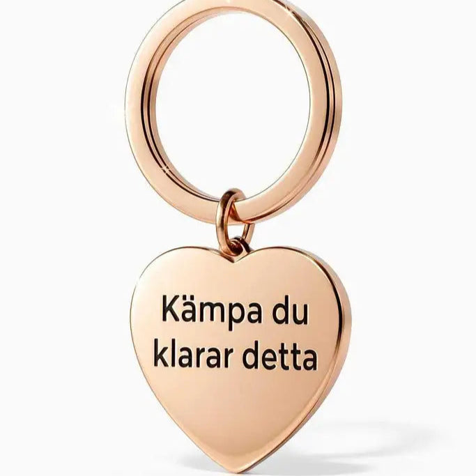 Nyckelring | Kämpa du klarar detta by Express-presenter är en guldfärgad, hjärtformad nyckelring i rostfritt stål med lasergraverad text: "Kämpa du klarar detta", vilket betyder "Fortsätt kämpa, du klarar det här.