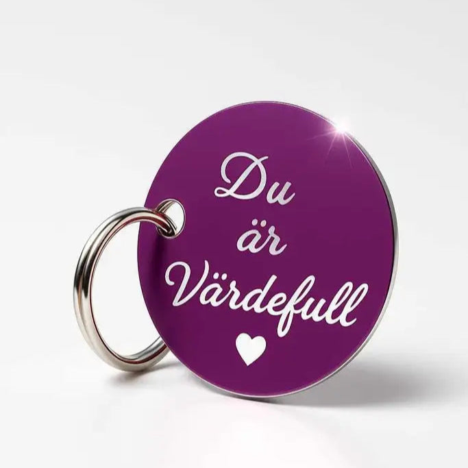Nyckelring | Du är värdefull (lila) från Express-presenter: mörklila, rund (40mm) med silverring, dekorerad med frasen "Du är värdefull" och ett litet vitt hjärta på ljus bakgrund.