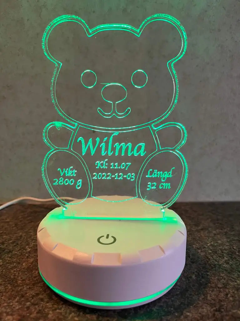 Express-presentatören Födelsetavla med info samt belyst är en glödande björnformad LED-lampa i akryl med gröna kanter, som visar "Wilma", födelsedatum 2022-12-03, tid 11:07, vikt 2800g och längd 32cm i vit text-en söt nattlampa med namn.