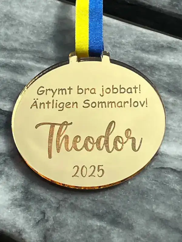 Sommarlovsmedalj |Grymt bra jobbat från Express-presenter, med ett blågult band, säger: Grymt bra jobbat! Äntligen Sommarlov! Theodor 2025, utställd på en grå marmoryta.
