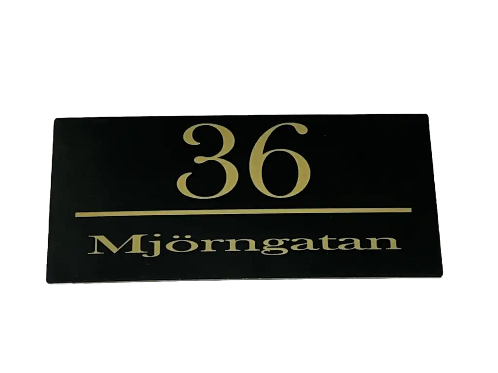 Express-presenter Postlådeskylt är en svart rektangulär 150×50 mm skylt med guldfärgad text som visar siffran 36 ovanför en linje och "Mjörngatan" under.