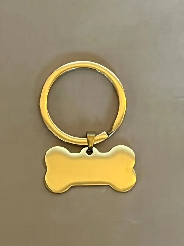 Expresspresenter.se Hundbricka är en nyckelring i guld med en blank, benformad tagg, perfekt som namnbricka till ett hundhalsband eller som en snygg accessoar, visad på en neutral bakgrund.