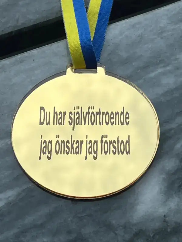 Medalj | Du har självförtroende by Express-presenter består av en 3mm spegelplast guldmedalj på ett blågult sverigeband, graverad med "Du har självförtroende jag önskar jag förstod".