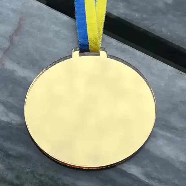 A blank gold "Medalj | Skapa din egen" från Express-presenter med blått och gult Sverigeband vilar på en grå marmoryta.