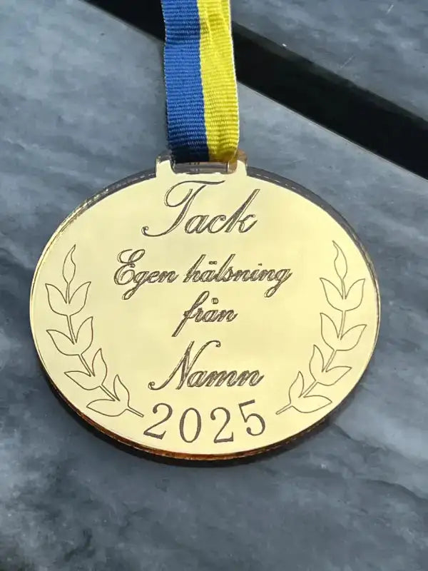 Medalj Tack egen hälsning från Express-presenter är en 3mm tjock spegelplast guldmedalj med lagerkvistar, blågult sverigeband, graverad med "Tack Egen hälsning från Namn 2025", visas på en grå yta.