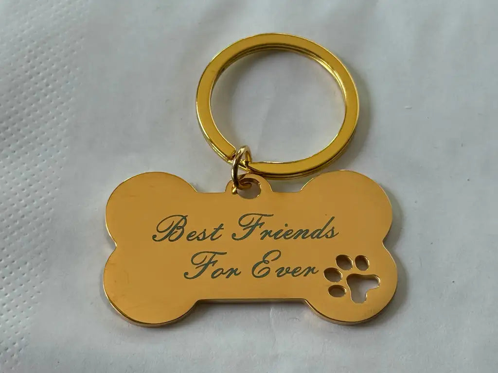 Nyckelringen "Hundben Best friends for ever" från Express-presenter i guld med text och tass, lasergraverad på rostfritt stål, ligger på en vit, texturerad yta.