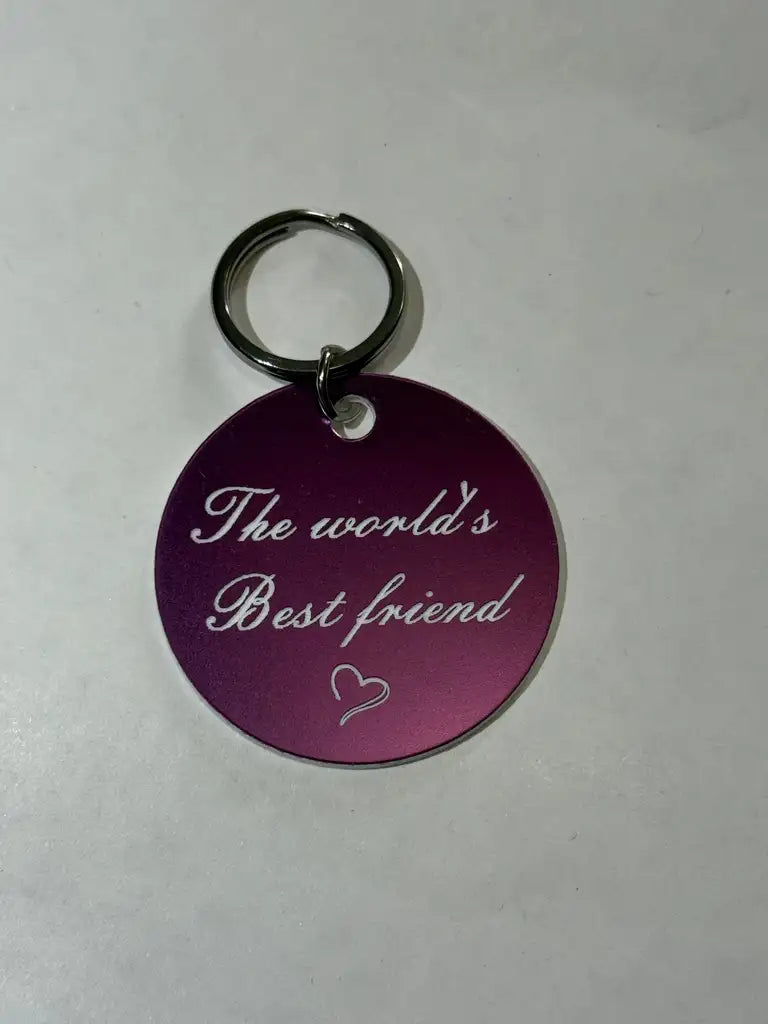 En rund, mörklila nyckelring (40mm) från Express-presenter med "The world´s best friends" och ett litet hjärta ingraverat, visad på en vit yta.
