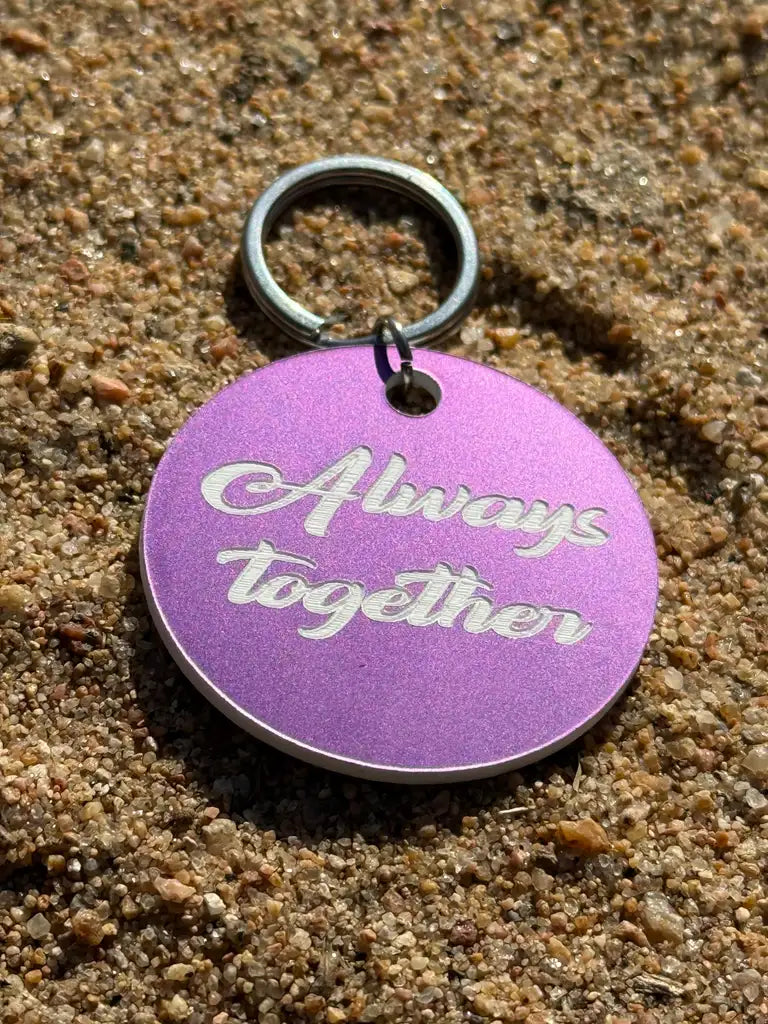 Express-presenter Nyckelring | Always together är en 40 mm rund, mörklila nyckelring med "Always together" ingraverat i vitt, avbildad på sandfärgad mark.
