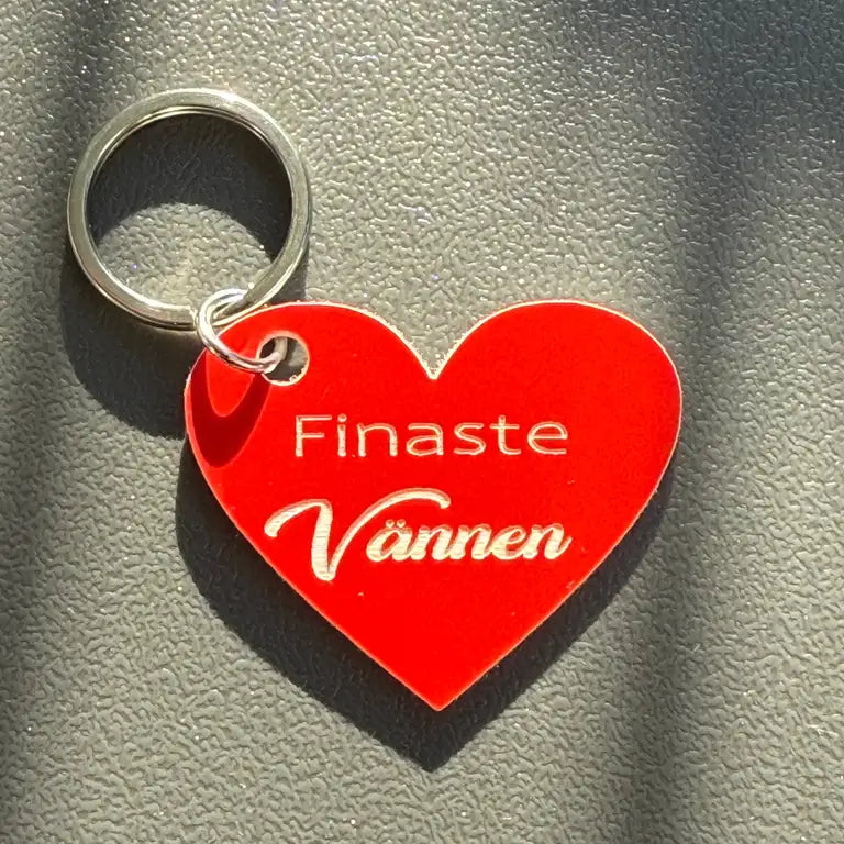 Nyckelring | Finaste vännen (röd) från Express-presenter - en hjärtformad röd nyckelring med vit gravyr, liggande på en texturerad grå yta med mjuka skuggor.