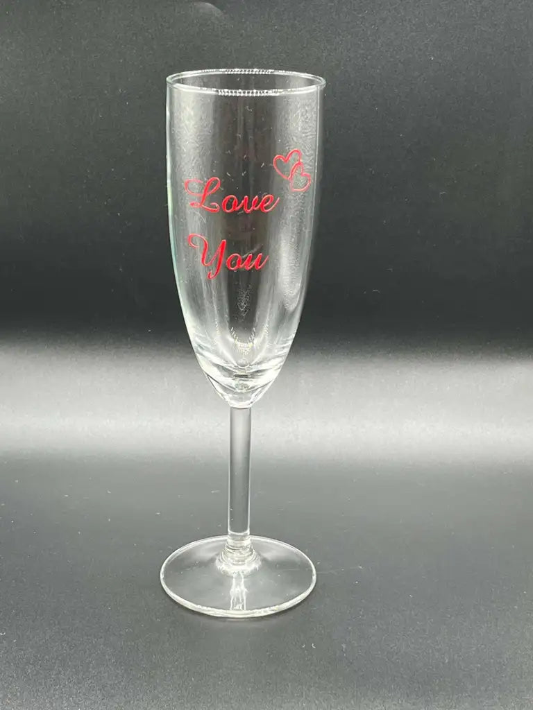 Champagneglas med text Love You från Expresspresenter.se - klart glas med röd vinyltext "Love You" och två röda hjärtan ovanför på svart bakgrund. Ett perfekt kärleksuttryck till någon speciell.