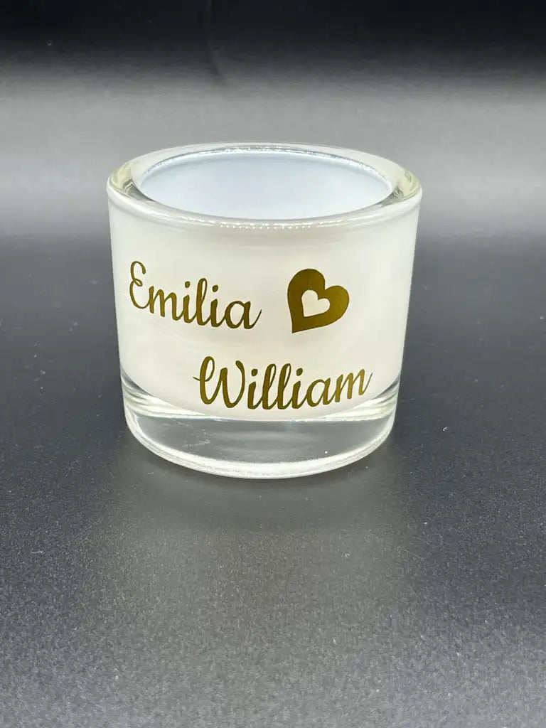 Ljuslykta med namn och hjärta från Expresspresenter.se - en glaslykta med namnen Emilia och William i guldskrift, åtskilda av ett guldfärgat hjärta mot mörk bakgrund.