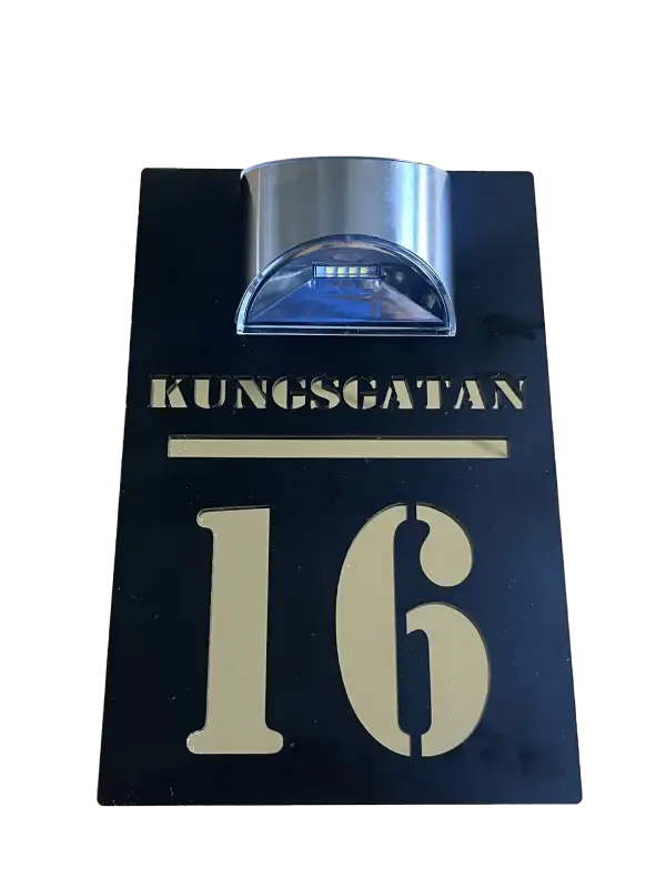 En svart rektangulär Husskylt solcellsdriven från Express-presenter med "KUNGSGATAN 16" i guld och en silverfärgad LED-solcellslampa på toppen för dekorativ belysning.