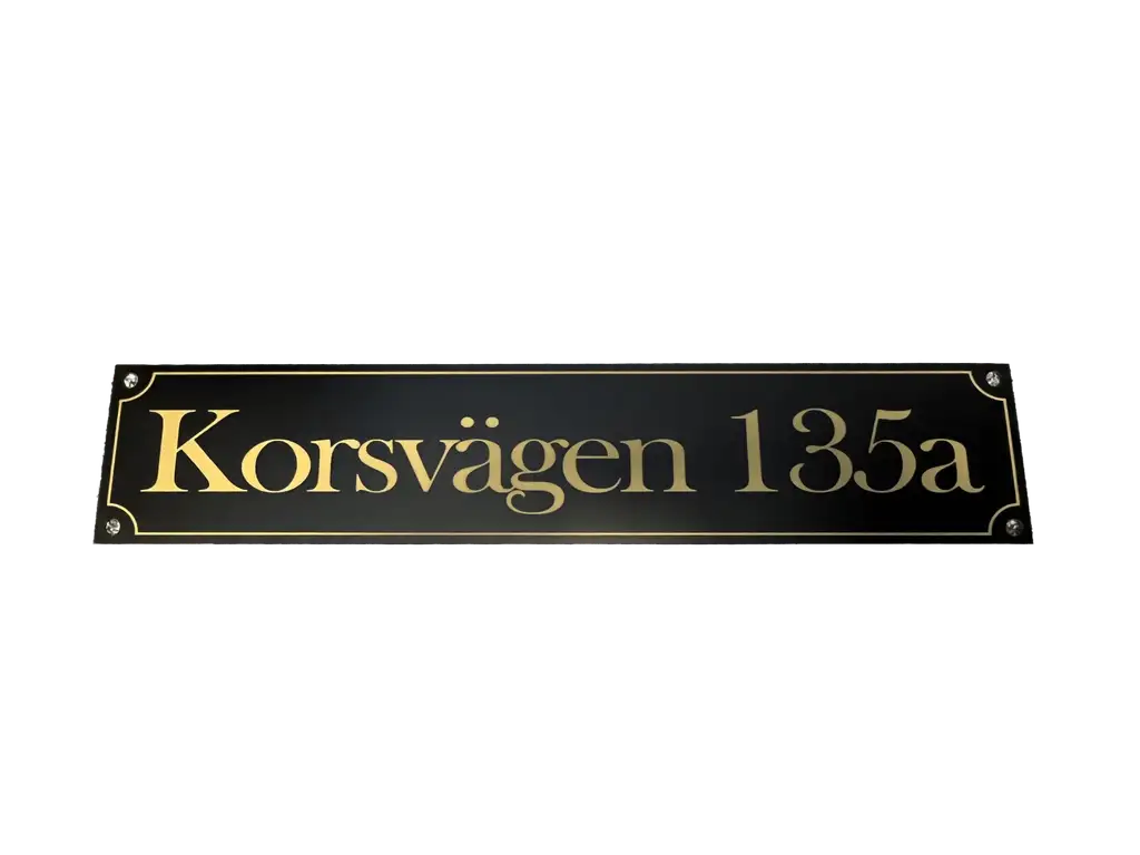 Express-presenter Adresskylt är en svart rektangulär skylt (300×100 mm) med guldtext "Korsvägen 135a", en tunn guldkant och fyra skruvhål i hörnen.