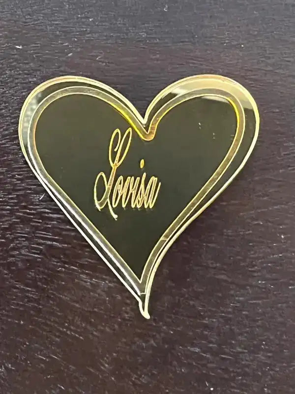Express-presenter's Bordsdekoration - en hjärtformad nål i guld med "Lovisa" i kursiv stil - ger elegans och charm till din dukning och är perfekt för att placera gästerna med stil på alla mörka träytor.