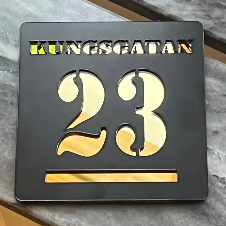 En svart Express-presenter Brevlådeskylt metallskylt med utskuren text med "KUNGSGATAN" högst upp och siffran 23 nedanför, placerad på en grå marmoryta.