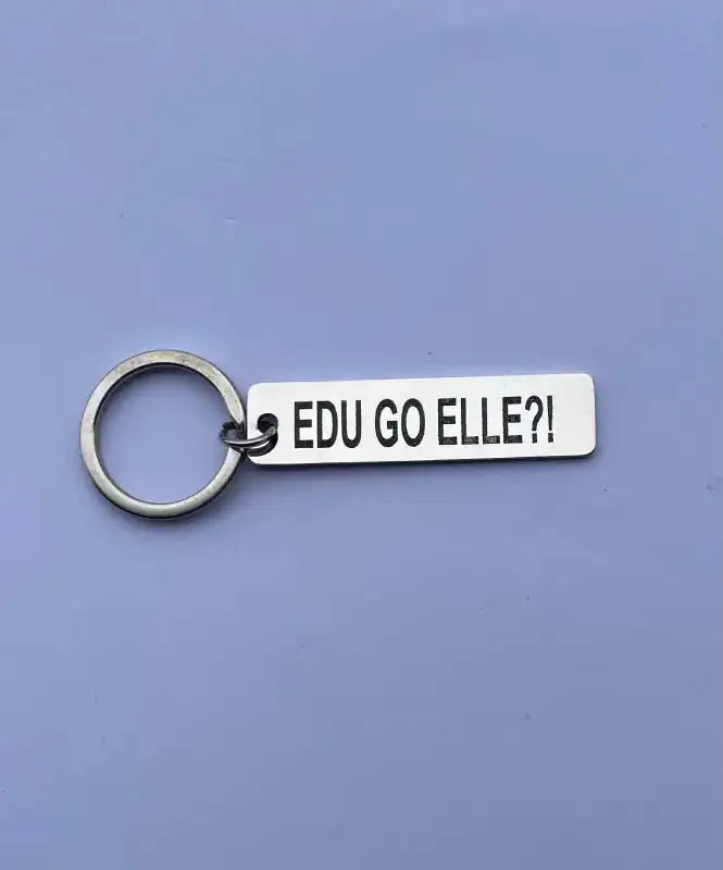 Expressens presentatör Nyckelring | EDU GO ELLE?! är en silverfärgad nyckelring med rektangulär tagg och lasergraverad svart versal text med texten "EDU GO ELLE?!" på en ljuslila bakgrund.