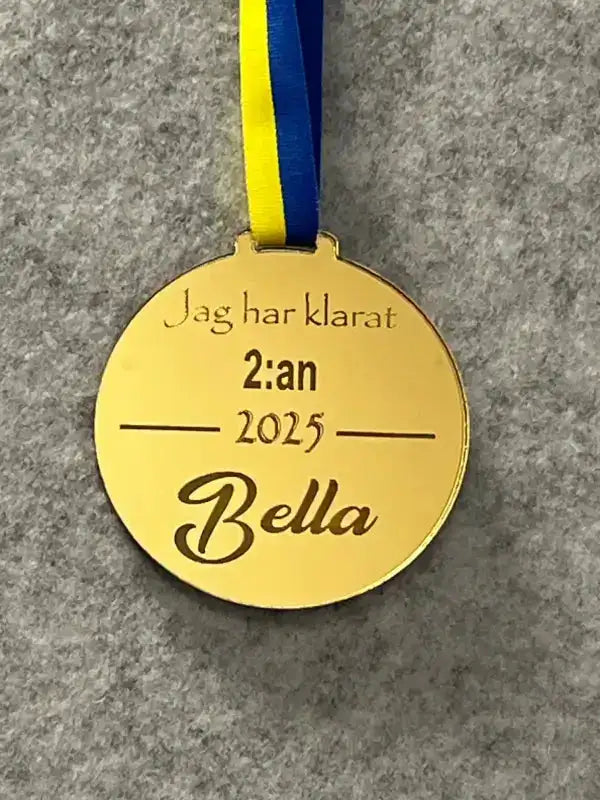 Express-presenter Medalj | Jag har klarat 2:an: Guldfärgad spegelplastmedalj med Sverigeband och texten "Jag har klarat 2:an 2025 Bella" mot grå bakgrund. Kan graveras med namn.