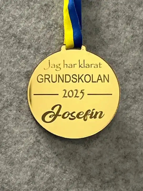 Expressens presentermedalj | Jag har klarat GRUNDSKOLAN är en guldspegelplastgraverad medalj med ett blått, gult och Sverigebandsband. Den har texten "Jag har klarat GRUNDSKOLAN 2025 Josefin" mot en grå bakgrund.
