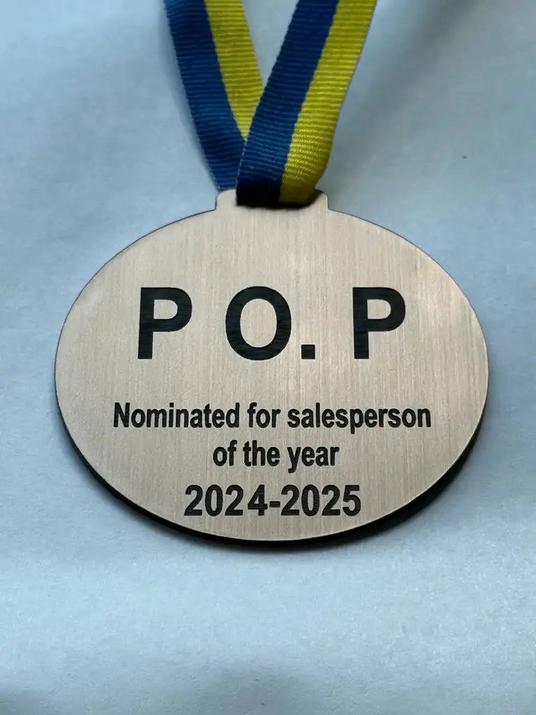 A Medalj Nominerad för bästa by Express-presenter, silver med blågult band, med texten "P.O.P Nominerad till årets säljare 2024-2025" mot ljus bakgrund.