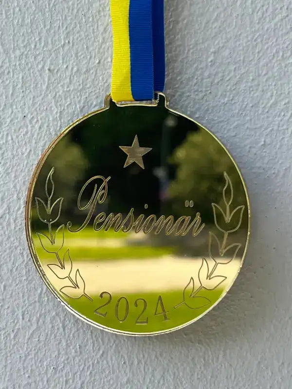 Medalj | Pensionär från Express-presenter med personligt årtal 2024 graverat på spegelplast guld, dekorerad med lagerkvistar och stjärna, hänger i blågult band mot ljus bakgrund.