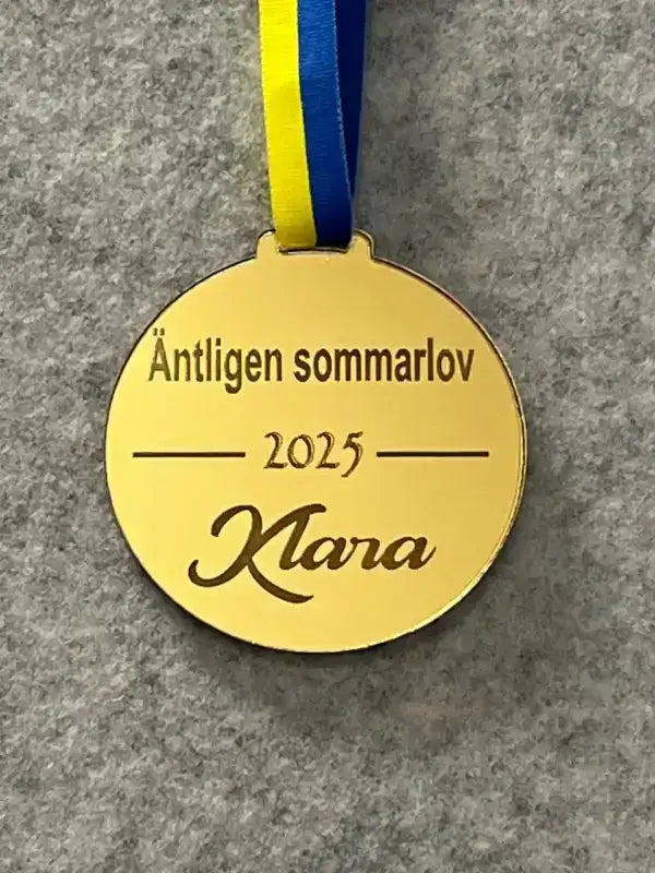 Medalj | Äntligen sommarlov med vågrät text från Express-presenter är en spegelplastmedalj med "Äntligen sommarlov 2025 Klara" ingraverat, hängande på ett blågult band mot en grå bakgrund.