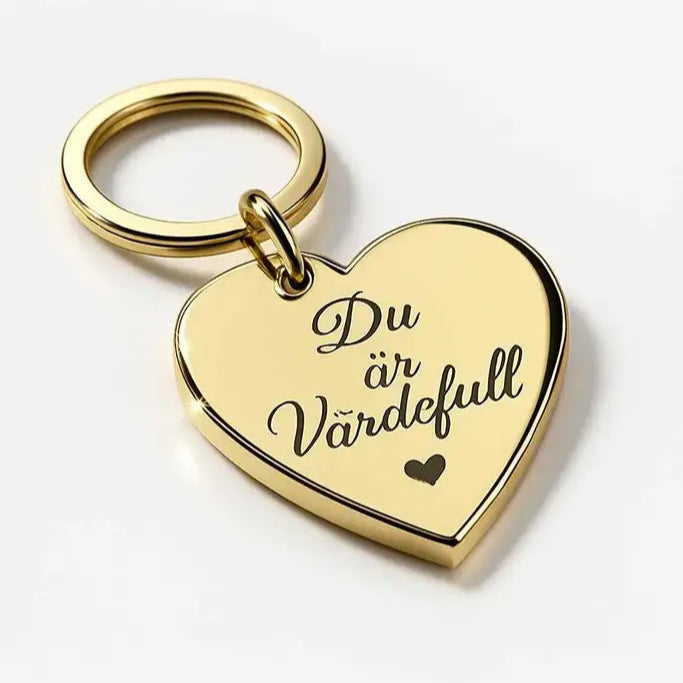 Nyckelringen - Du är värdefull by Express-presenter är en 4x3cm guldfärgad hjärtformad nyckelring tillverkad av 3mm spegelplast, graverad med ett litet hjärta och den svenska frasen "Du är värdefull" på en vit yta.