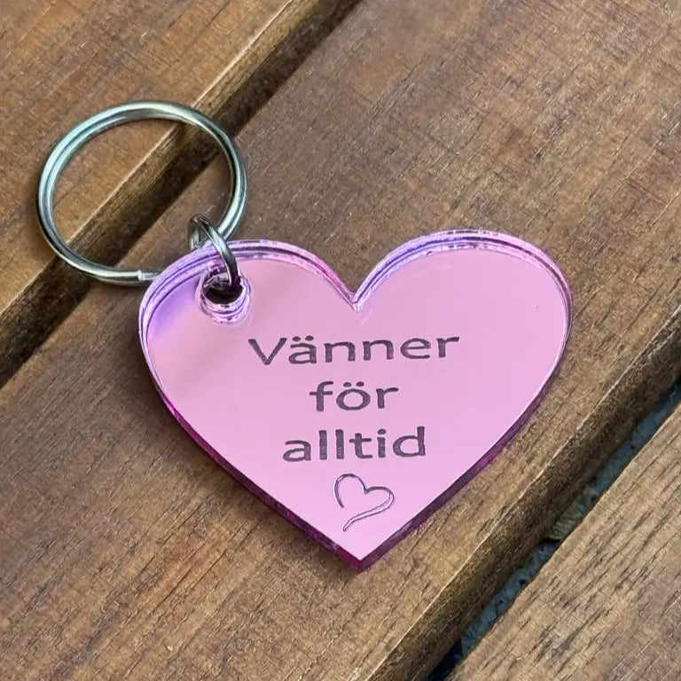 Nyckelring - Vänner för alltid (Rosa) från Express-presenter är en 4x3cm rosa, hjärtformad nyckelring i 3mm spegelplast med "Vänner för alltid" och en liten hjärtsymbol på, visad på en träyta.