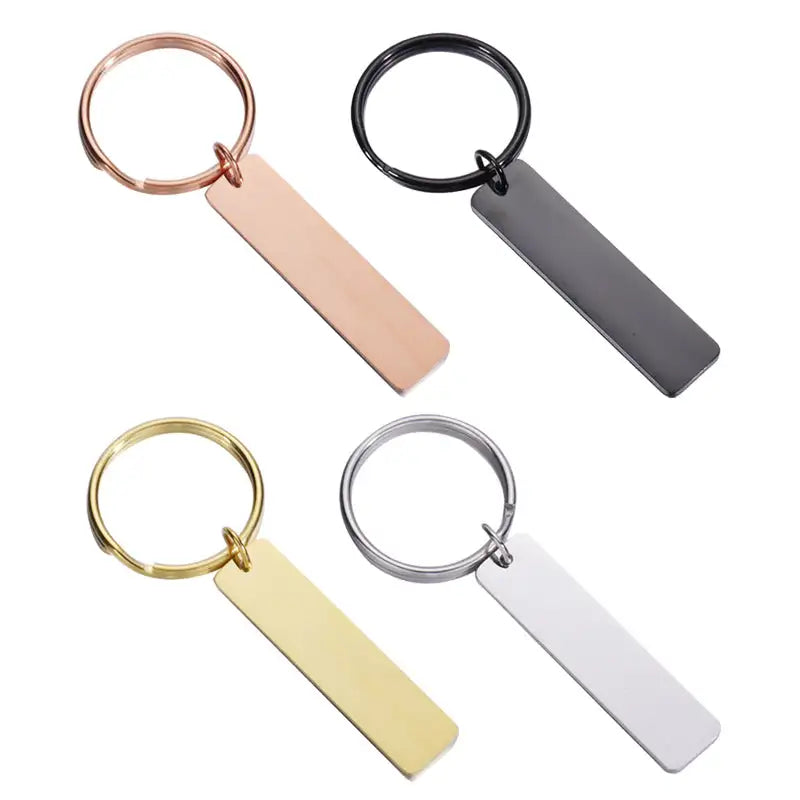 Fyra rektangulära nyckelringar-rose gold, svart, guld och silver-från Express-presenter visas på vitt underlag. Varje Nyckelring | Anpassningsbar i rostfritt stål har en platt tag och matchande ring för personlig stil.