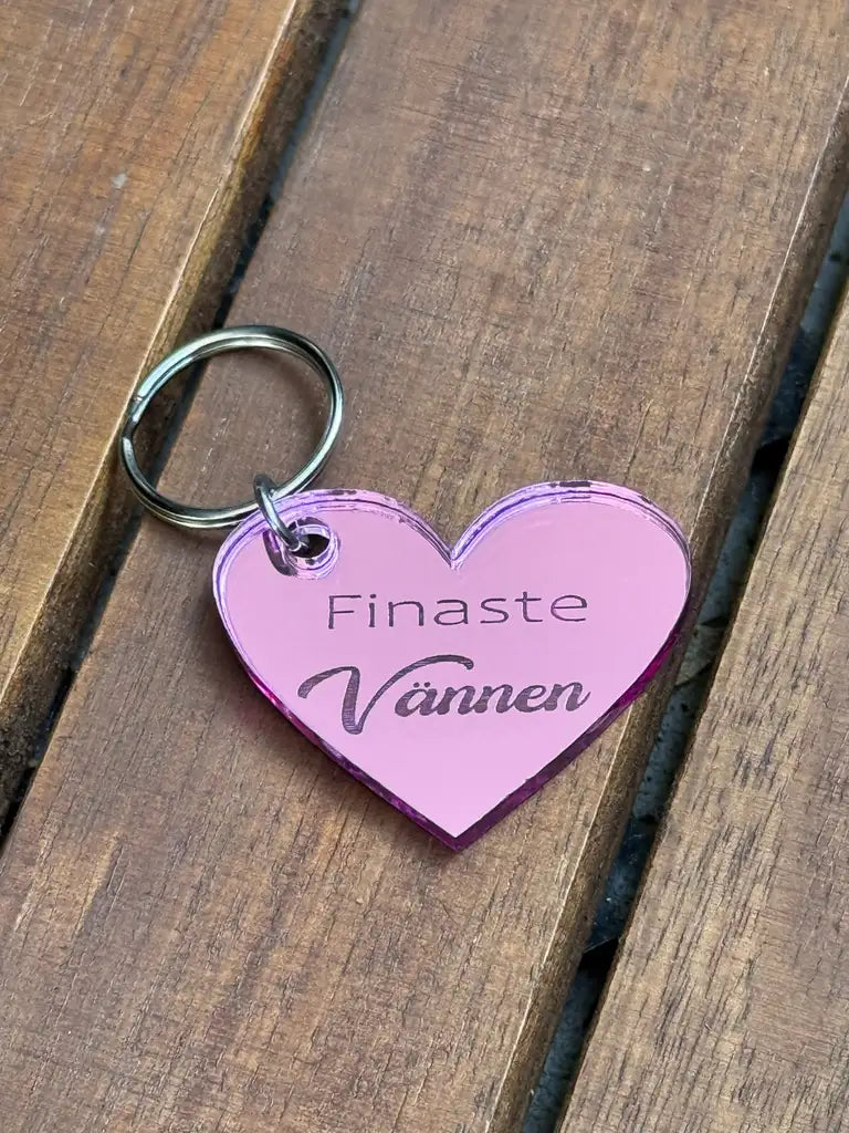 Nyckelring | Finaste vännen Rosa från Express-presenter - en hjärtformad nyckelring i rosa spegelplast med texten "Finaste Vännen", perfekt present till en vän, ligger på en träyta.