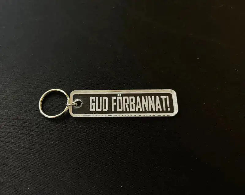 Nyckelringen GUD FÖRBANNAT från Express-presenter är en rektangulär nyckelring i akryl med en metallring, med "GUD FÖRBANNAT!" i fet vit på svart och en graverad baksida för extra unikhet.