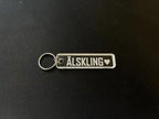 Nyckelringen | Älskling by Express-presenter är en rektangulär nyckelring i akryl med en silverring, graverad med "ÄLSKLING" och en hjärtsymbol, som visas på en svart yta.