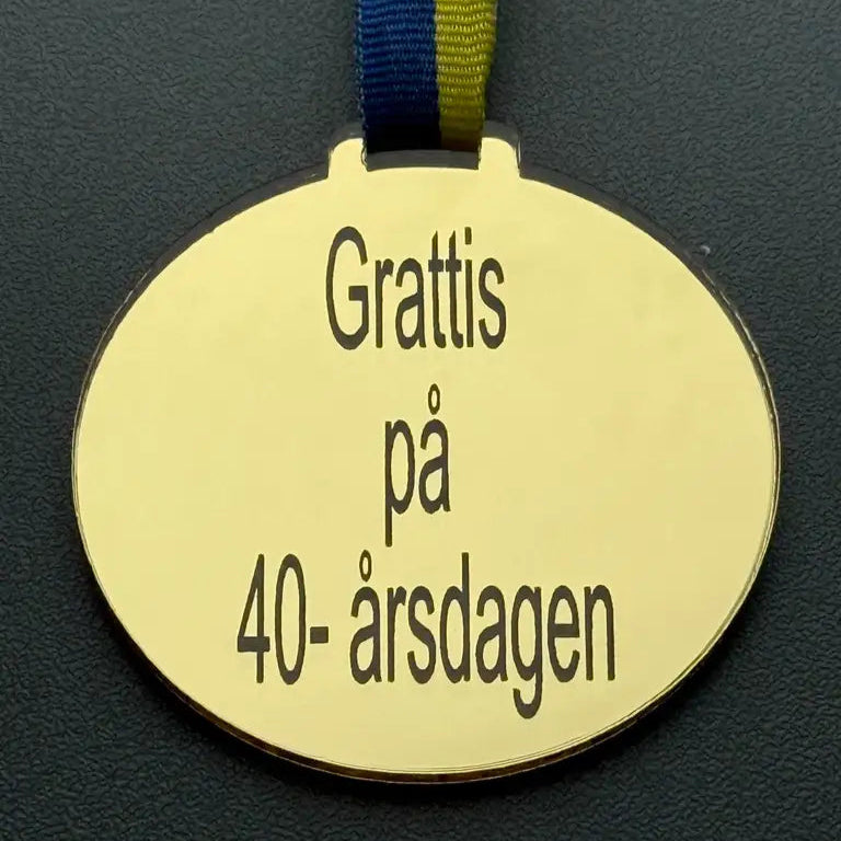 Expressens Presenter's Medalj | Grattis på 40-årsdagen: en guldmedalj i spegelplast guld med blågult band (70 x 3 mm), graverad med den svenska texten "Grattis på 40-årsdagen".