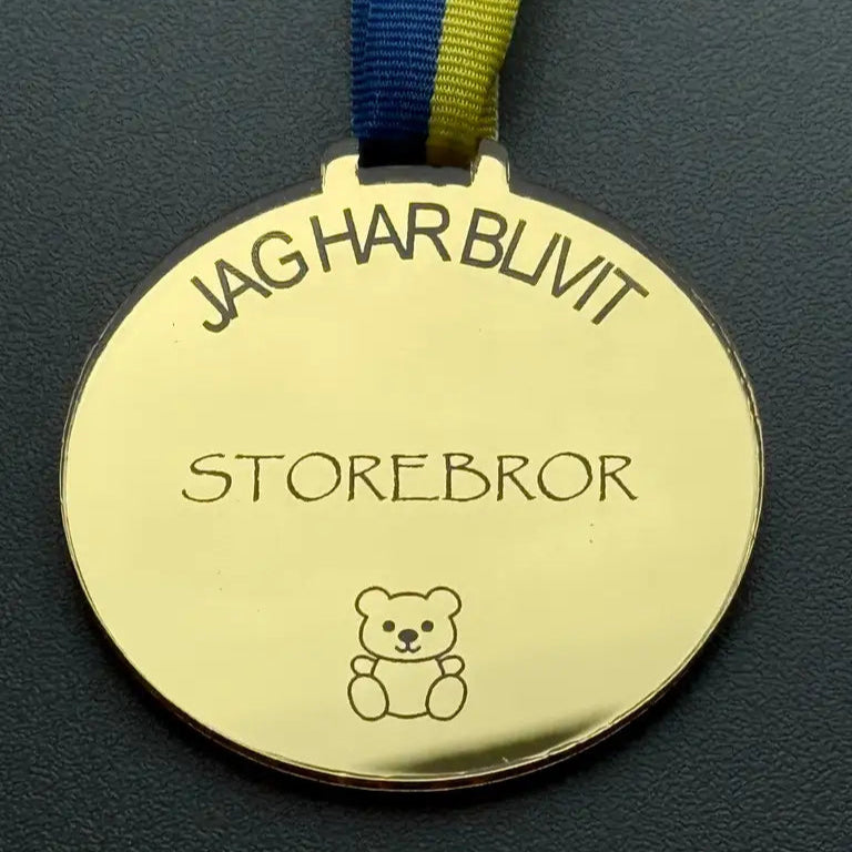 Medalj | Jag har blivit storebror från Express-presenter - en guldfärgad spegelplastmedalj med blågult band, graverad med "JAG HAR BLIVIT STOREBROR" och dekorerad med en nallebjörn.