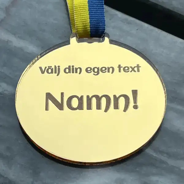 Medaljen Välj din egen text by Express-presenter är en guldmedalj med blågult sverigeband, tillverkad i spegelplast och graverad med texten "Välj din egen text Namn!".