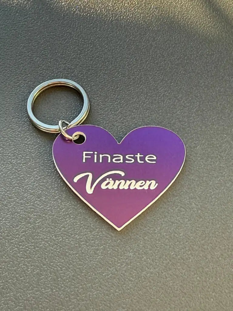 Nyckelring | Finaste vännen (lila) från Express-presenter är en hjärtformad lila nyckelring med vit gravyr "Finaste Vännen", placerad på en grå yta.