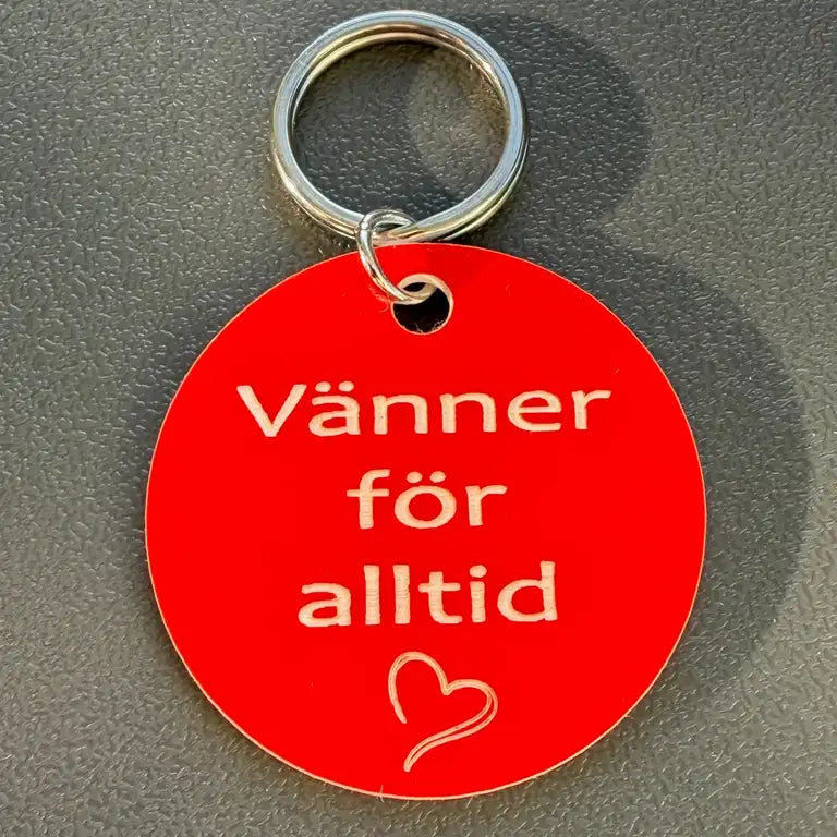 Express-presenter Nyckelring | Vänner för alltid (Röd), 40 mm och graverad med "Vänner för alltid" samt ett vitt hjärta, visas på en strukturerad grå yta.