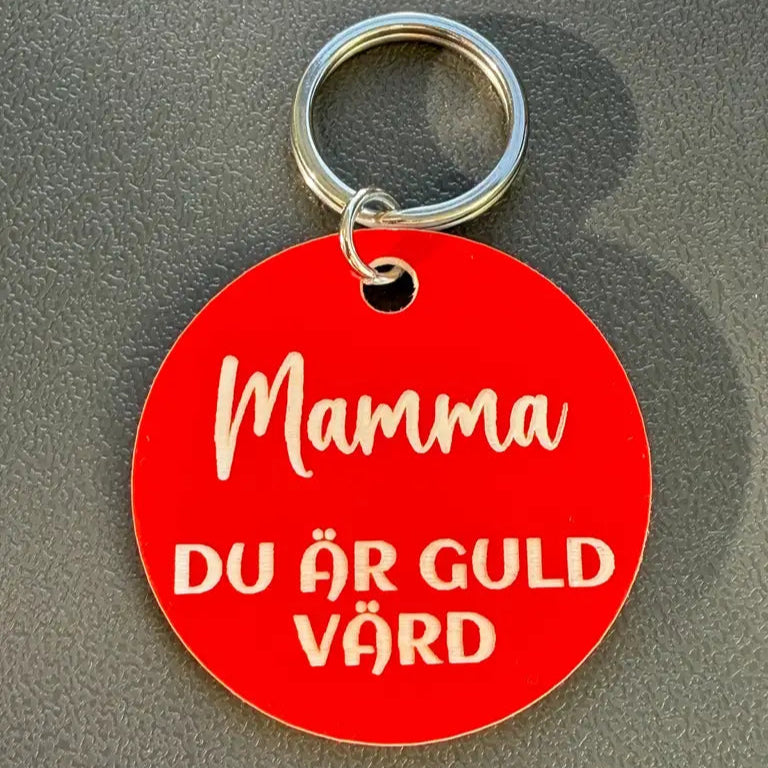 Nyckelringen Mamma du är guld värd (Röd) från Express-presenter är en 40mm rund röd plastnyckelring med vit svensk text och en silverfärgad nyckelring, visad på en grå yta.