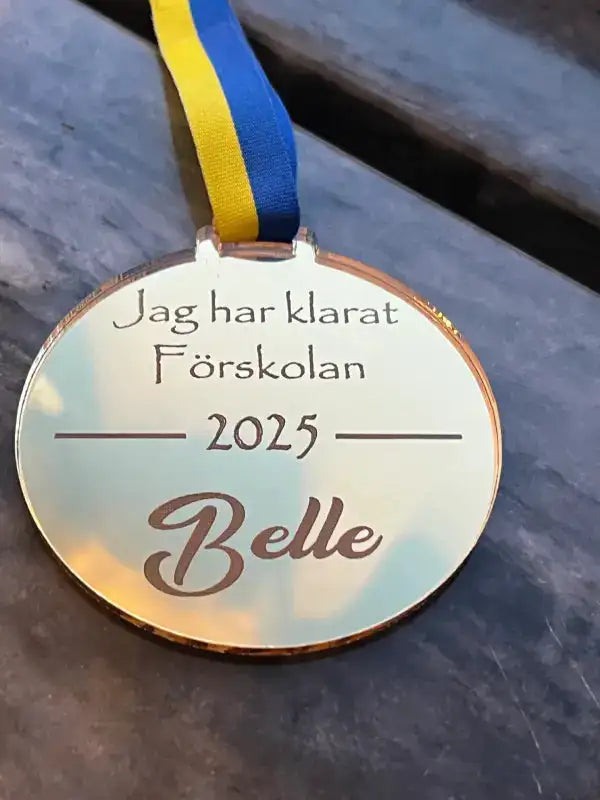Expressens Stilren Medalj | Förskolan är en guldfärgad medalj med blågult band och den svenska texten "Jag har klarat Förskolan 2025 Belle" - en perfekt personlig present för att fira denna milstolpe.