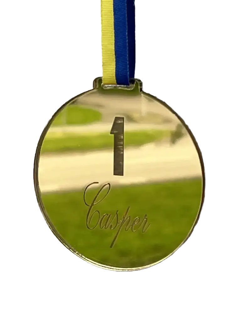 Express-presentatörens "Medalj | No 1" i spegelplast guld, med blågult band och "Casper" ingraverat, speglar den grönvita utomhusbakgrunden.