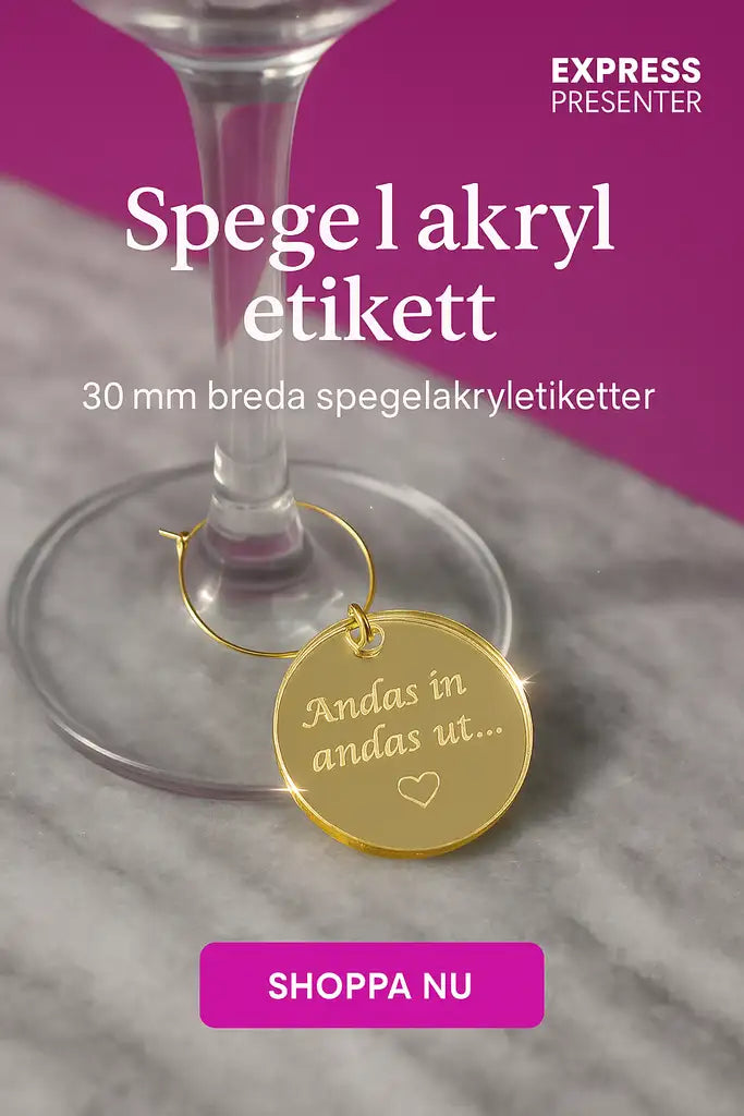 En Dekoration till glas från Expresspresenter.se - en guldspegel akryl etikett graverad med "Andas in andas ut..." - hänger på en vinglasstång ovanpå marmor. Ovan på bilden: "30 mm etikett" och en rosa "SHOPPA NU"-knapp.